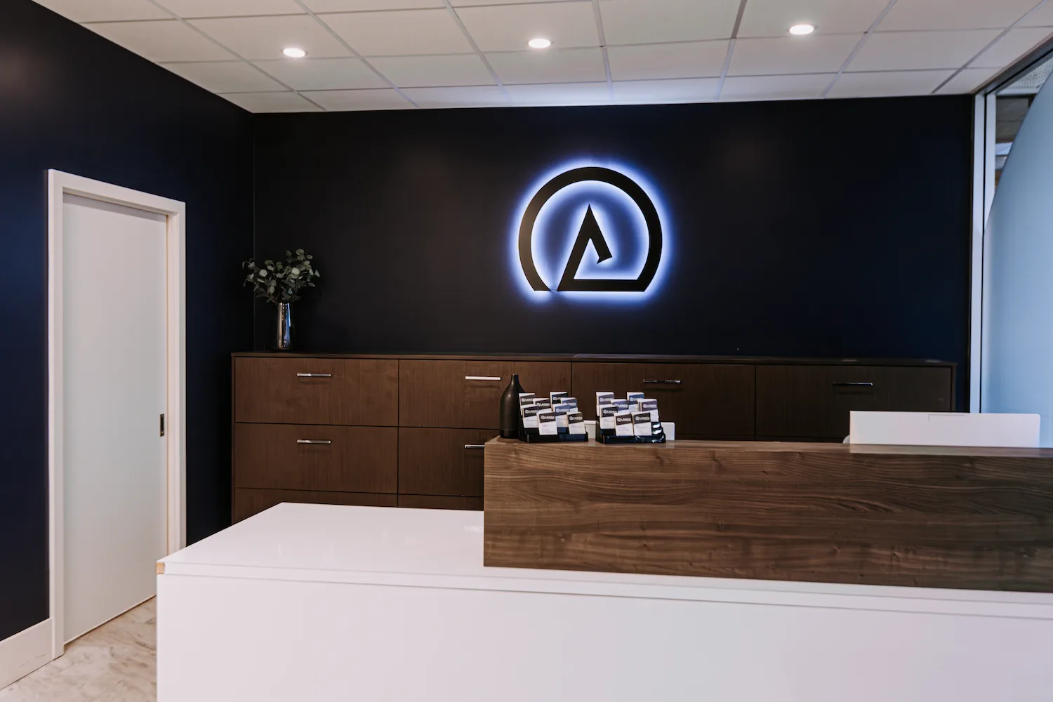 Reception desk at Launch Rehab North Burnaby with the backlit logo on a navy feature wall