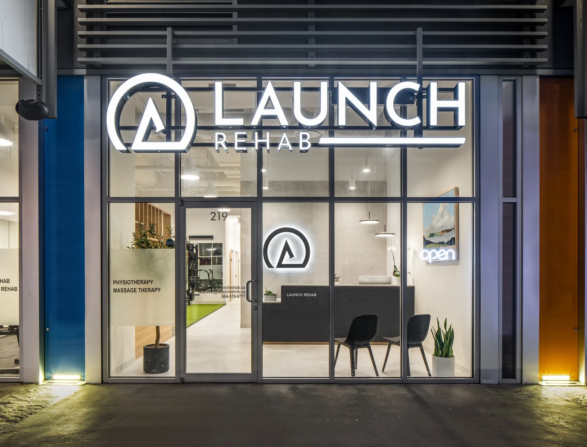 Launch Rehab New Westminster storefront at night with the illuminated logo above the entrance at Shops at New West